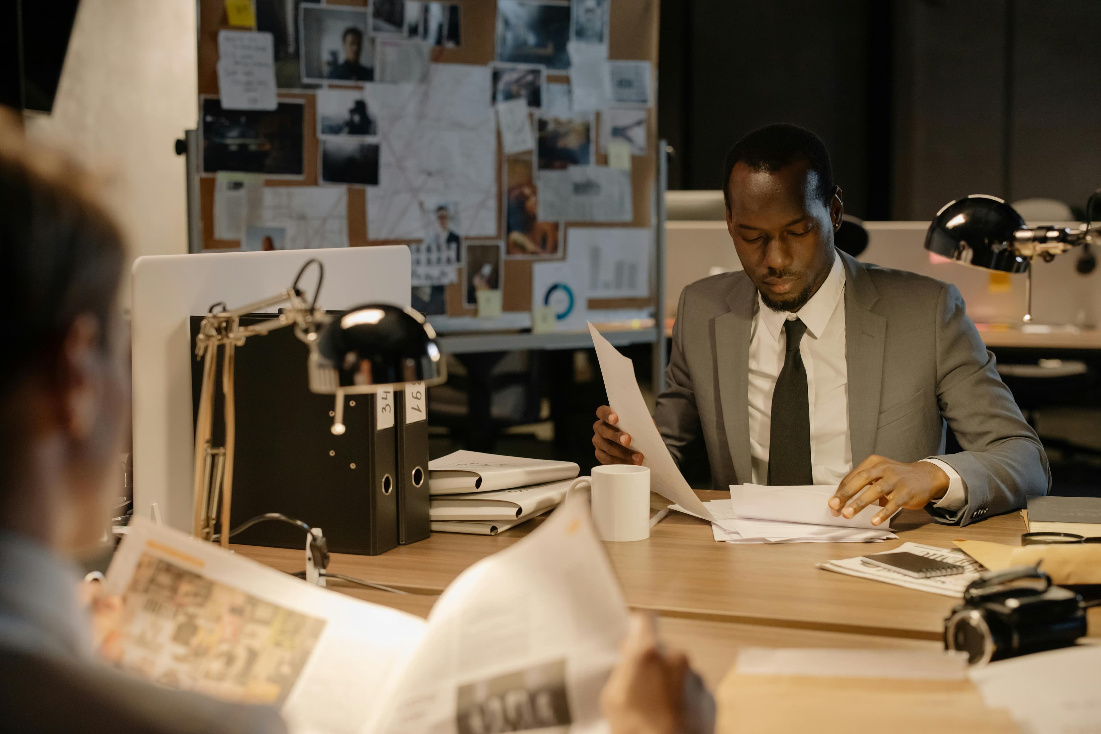 Man in a gray suit reviewing papers at a desk in front of a case board