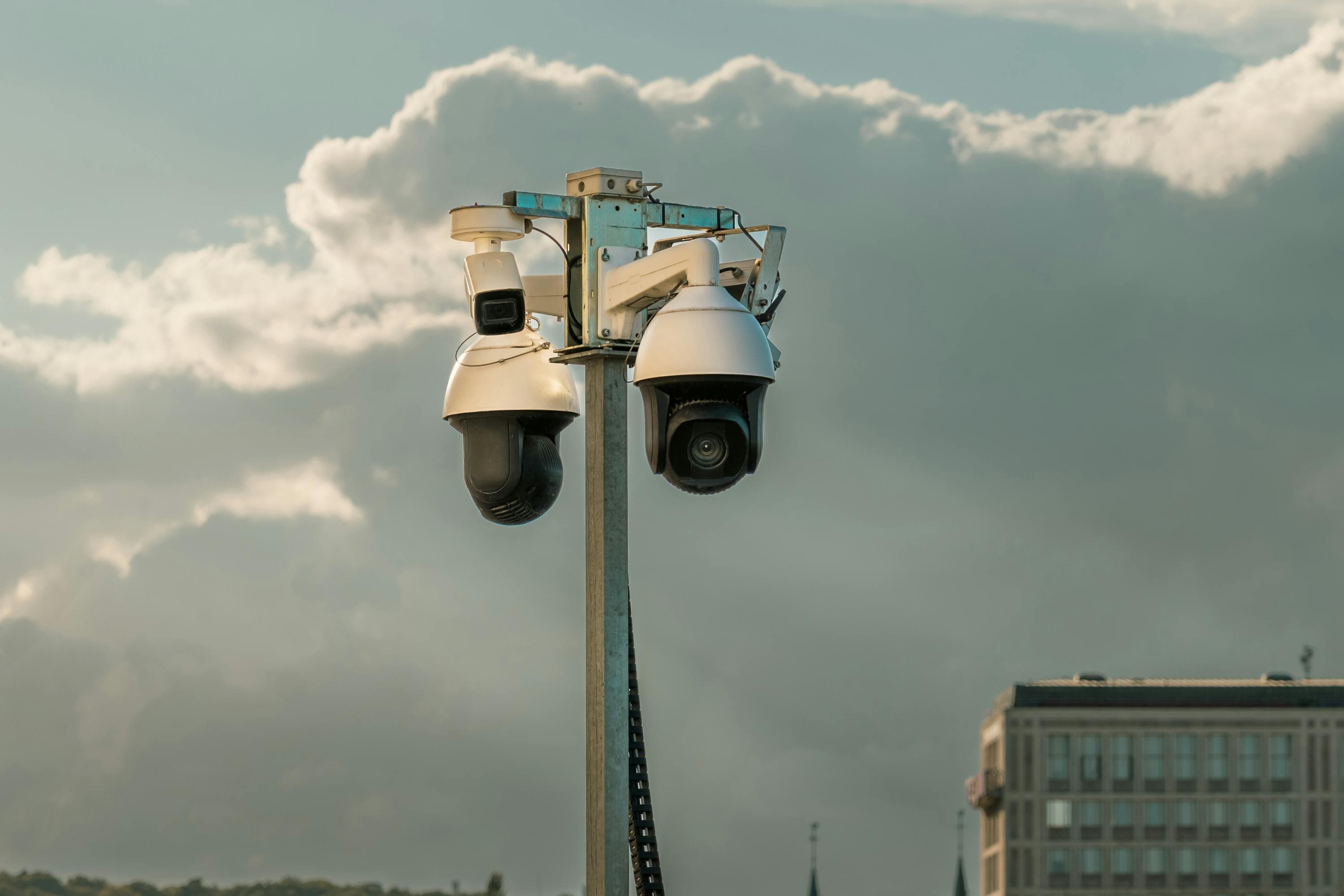 Security cameras mounted on a pole against a cloudy sky